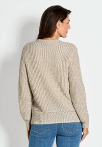 Beige gebreide trui met een geribbelde textuur, brede mouwen en een ronde halslijn, gecombineerd met blauwe jeans. Zicht vanaf de achterkant.