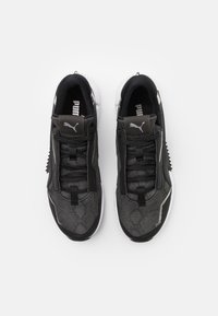 Ett par svarta och grå Puma-sneakers med vita sulor och svarta snören, sett ovanifrån på en vit bakgrund.