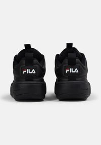 Baskets noires avec une tige en cuir lisse et en mesh, dotées d'une épaisse semelle en caoutchouc et d'une languette de talon en boucle. Logo Fila affiché de manière proéminente.