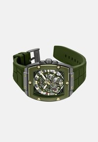 Grüne Silikonarmbanduhr mit einem quadratischen Gehäuse aus Edelstahl, transparentem Zifferblatt, sichtbaren Zahnrädern und goldenen Akzenten. Verfügt über einen silbernen Verschluss.