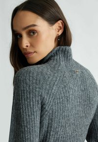 Maglione grigio a collo alto a coste realizzato in materiale morbido, con un collo alto e un piccolo logo sul retro.