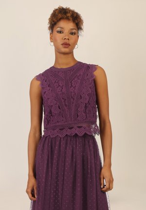 Lila Spitze Bluse mit gewellten Kanten und floralen Mustern, kombiniert mit einem transparenten Polka-Dot-Rock. Zarte und geschichtete Gestaltung.