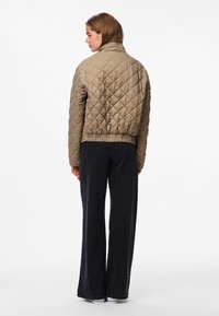 Jaqueta bomber acolchoada em verde-azeitona com colarinho alto, cintura elástica e um acabamento texturizado. Combinada com calças largas pretas e tênis.