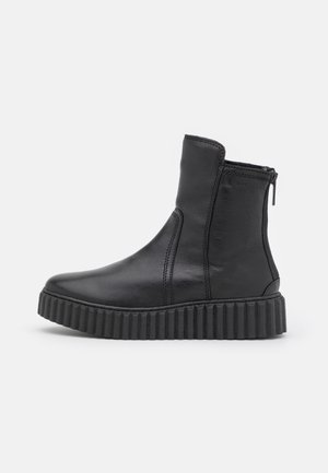 Schwarzer lederner Stiefel bis zur Mitte der Wade mit dicker, gerillter Sohle und seitlichem Reißverschluss, seitlich auf einem schlichten hellen Hintergrund gezeigt.