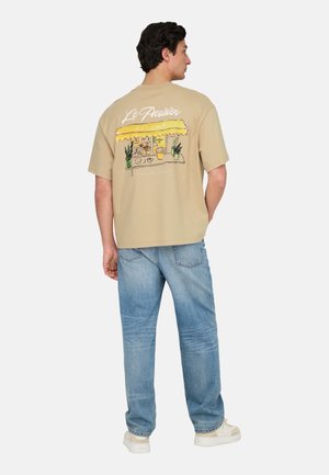 T-shirt oversize beige con una grafica colorata di un bistro con una tenda gialla, piante e testo scritto a mano sul retro.