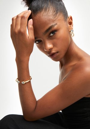 Ensemble de bijoux en ton or avec des pierres précieuses bleues en forme de triangle. Comprend des boucles d'oreilles et un bracelet en manchette avec des détails complexes.