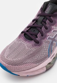 Gros plan d’une chaussure de course Asics rose et violette avec une tige en mesh texturé, des lacets à motifs et un détail bleu sur la semelle extérieure.