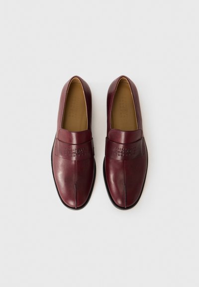 Par av vinröda läder slip-on loafers med svarta sulor, med embossad logotyp och nummerserie-design på de övre remmarna.