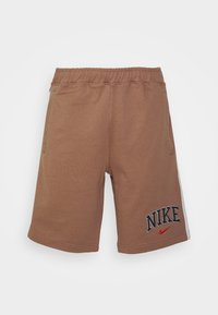 Bruna Nike-shorts med resårmidja, med ett broderat logo och en röd Nike-swoosh på framsidan, mot en vit bakgrund.