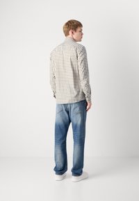 Camicia a quadri marrone chiaro e bianca con colletto, abbinata a jeans in denim blu chiaro e sneakers bianche, vista da dietro.