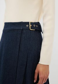 Mörk marinblå kjol med ränder som har en bred midjeband, gyllene spänne och diskreta sidofållor. Mjuk tygtextur med skräddarsydd design.