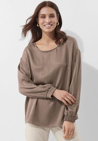 Lässige braune Bluse mit langen Ärmeln, elastischen Bündchen, Rundhalsausschnitt und glatter Textur. Sichtbares Stichdetail vorne.