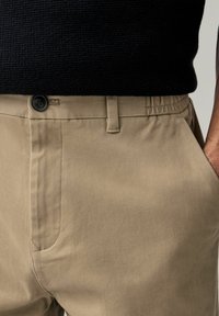 Beesidist valmistatud pehmetest kangast beezid chinos püksid, millel on nööp sulgemine, küljetaskud ja elastne vöökoht mugavuse tagamiseks.