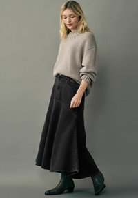 Grå striktrøje med rullede manchetter parret med en lang sort denimskirt med paneldetaljer og en udvidet silhuet. Grønne ankelstøvler.