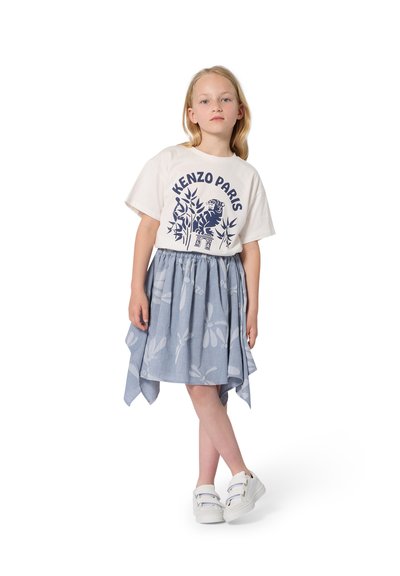 T-shirt blanc Kenzo Paris avec motif bleu, associé à une jupe bleue à motif floral et à un ourlet asymétrique. Baskets blanches.