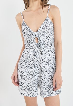 Biały kombinezon w kwiaty z głębokim dekoltem w kształcie litery V, cienkimi ramiączkami i wiązaniem z przodu. Posiada małe granatowe kwiaty i luźny krój.