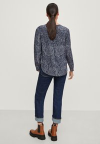Blusa a fantasia navy con maniche lunghe, abbinata a jeans blu scuro risvoltati e stivali alla caviglia marroni con suole nere e lati elasticizzati.