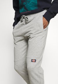 Pantaloni della tuta grigio chiaro realizzati in tessuto misto cotone, con elastico in vita, tasche laterali e un patch del logo del brand cucito sulla coscia.