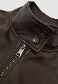 Guler de geacă din piele maro cu textură netedă. Prezintă un fermoar argintiu și două nasturi închiși la culoare aproape de gât. Detalii de design sofisticate.