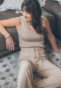 Beige geripptes Tanktop, kombiniert mit hoch taillierten, weit geschnittenen Hosen mit einem Bindegürtel. Weicher Stoff, der auf einem leicht gemusterten Teppich liegt.