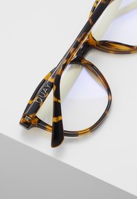 Gafas de sol carey con un marco grueso, que cuentan con un forro interior transparente y un logo plateado "QUAY" en la patilla.
