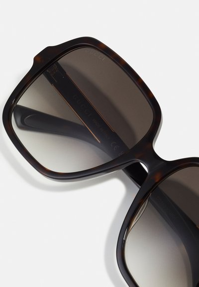 Occhiali da sole Gucci con grandi montature quadrate in tartaruga scura, dotati di lenti grigie sfumate e un sottile dettaglio del marchio sulla stecca.