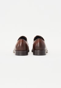 Scarpe in pelle marrone con una texture liscia, punta arrotondata e tacco basso impilato. Presentano un design senza cuciture senza hardware visibile.
