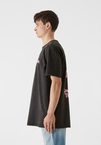 Črna oversize majica iz bombaža. Na sprednji strani ima roza besedilo. Ima kratke rokave in okroglo izrez. Lahka, sproščena kroja.