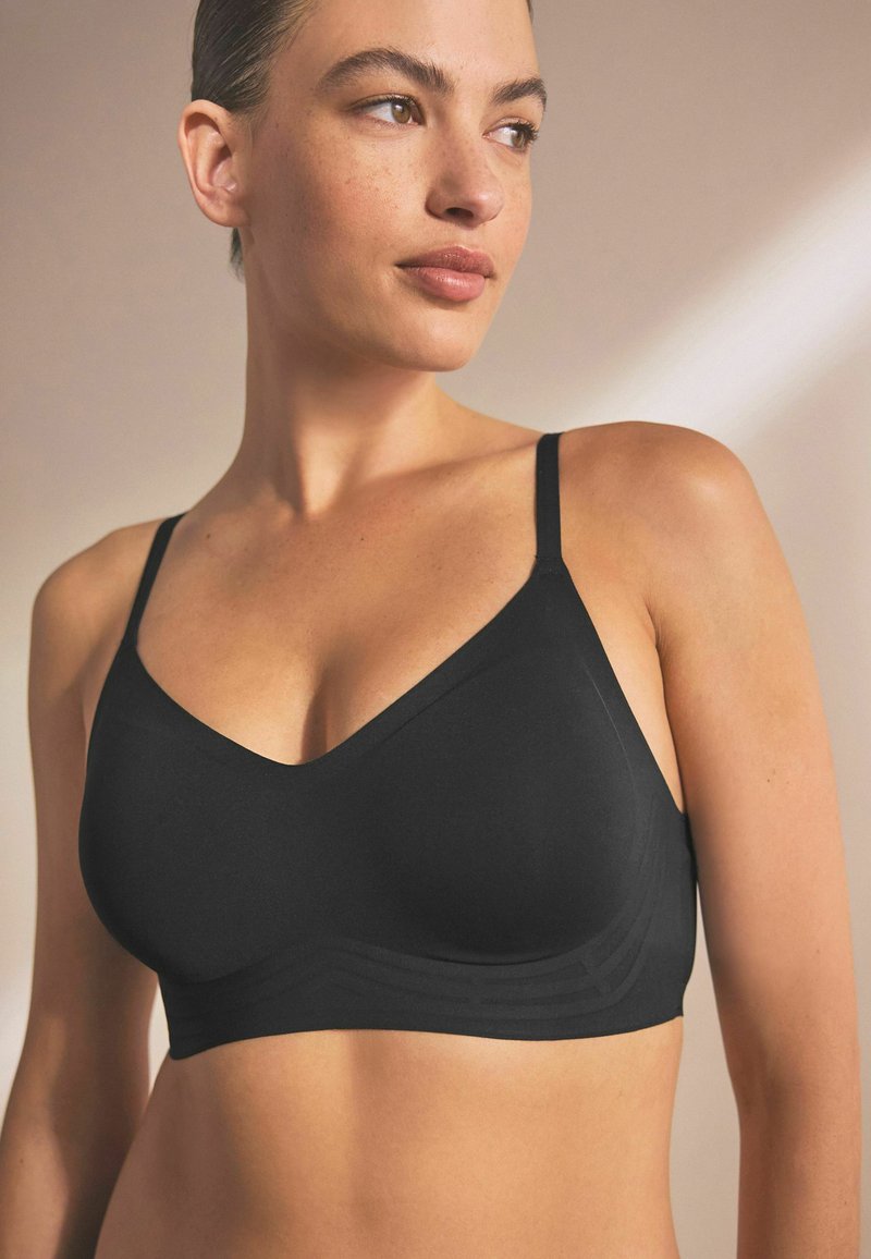 Black, wireless bralette with a V-neck design, adjustable straps, and textured lower band. Smooth fabric with a fitted silhouette.