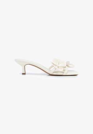 White heeled mule sandal with kitten heel and two large decorative flower appliques on the straps.