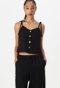 Svart kort topp laget av lin med justerbare knytestrikker og fem knapper foran, sammen med elastiske svarte bukser.