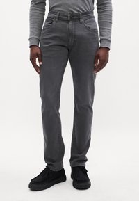 Jeans in denim grigio con vestibilità dritta, dotati di cinque tasche e chiusura con bottone. Indossati con scarpe nere, mostrano una trama liscia.