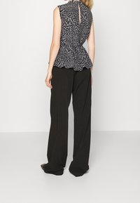 Top peplum senza maniche bianco e nero con motivo floreale, dettaglio a oblò sulla schiena, abbinato a pantaloni neri a gamba larga. Tessuto dalla texture liscia.