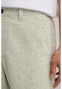 Light green striped trousers made of soft fabric, featuring a waistband with a button closure and side pockets for functionality.