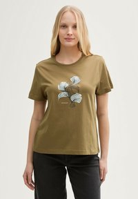 T-shirt en coton vert olive avec un motif floral en noir et blanc, col rond et manches courtes. Coupe décontractée avec une texture lisse.