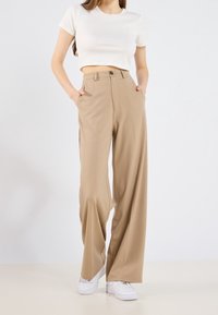 Beige wijde broek met voorzakken, sluiting met één knop en zijnaaddetails, gecombineerd met een witte cropped t-shirt en witte sneakers.