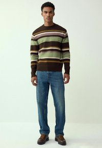 Brown, green, and cream striped knit sweater with ribbed cuffs, paired with blue straight-leg jeans and brown lace-up boots.
