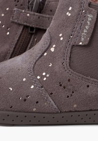 Stivale alla caviglia in suede grigio con paillettes metallizzate, pannello laterale elastico e suola in gomma testurizzata con perforazioni. Chiusura con zip sul lato.