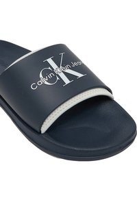 Chancla de color azul marino hecha de material sintético con una correa acolchada y costuras blancas, que presenta un gran logo impreso en blanco.