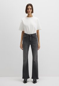 White short-sleeve t-shirt paired with high-waisted, flared black jeans. The jeans feature a classic five-pocket design and subtle fading.