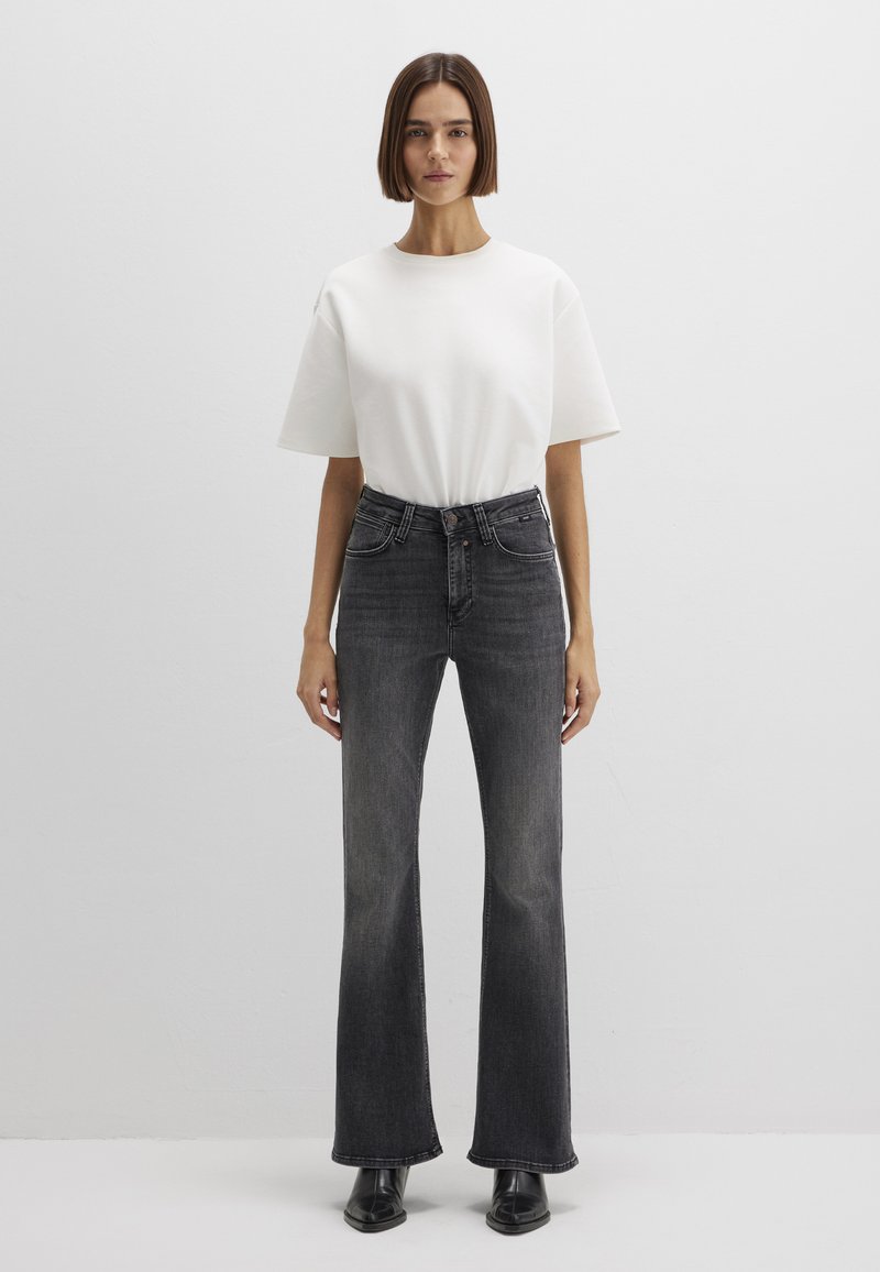 White short-sleeve t-shirt paired with high-waisted, flared black jeans. The jeans feature a classic five-pocket design and subtle fading.