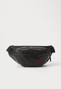 Juodas fanny pack'as, pagamintas iš blizgaus medžiagos, su apvaliu dizainu, turintis raudoną logotipo pleistrą ir reguliuojamą diržą saugiam dėvėjimui.