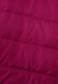 Gros plan sur un motif matelassé horizontal cousu sur un tissu magenta, montrant la texture et les sections rembourrées.