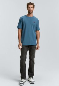 Šviesiai mėlynas medvilninis marškinėlis trumpomis rankovėmis, laisvo silueto. Derinamas su tamsiais džinsais ir sportbačiais, turi balto bei tamsiai mėlyno akcentus.