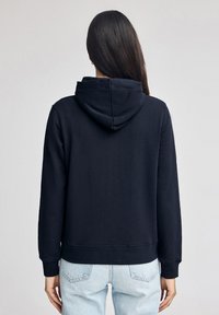 Sudadera marina con un bolsillo tipo canguro, puños y dobladillo acanalados, que presenta una capucha amplia. El material parece suave y ligeramente texturizado.