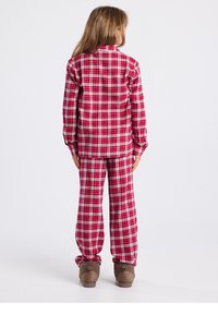 Rode geruite flanellen pyjama set met een longsleeve top en bijpassende losse broek. Heeft een gestructureerde stof en wordt gecombineerd met bruine slippers.