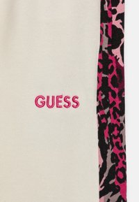 Lys beige bukser med et pink broderet "GUESS" logo. Sidepanelet har et pink og sort leopardmønster. Blødt bomuldsstof.