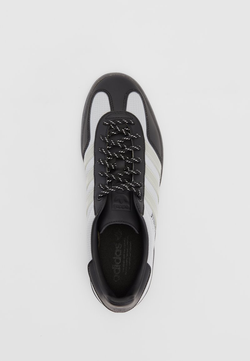Schwarz-weißer Sneaker aus Netz- und Lederstoffen, mit gepolstertem Zungenbereich, schwarzen Schnürsenkeln und drei weißen Streifen an der Seite.