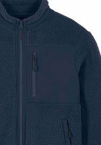 Veste polaire bleu marine à surface texturée, dotée d'un col haut, de deux poches zippées et d'accents en tissu lisse.