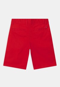 Rote knielange Shorts mit Gürtelschlaufen, zwei Gesäßtaschen mit Paspel, und einem kleinen rechteckigen Logo im Bereich der rechten Tasche.